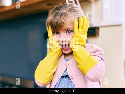 Oh pas le temps de laver la vaisselle. Portrait d'une petite fille à la recherche surprise tenant son visage avec ses mains tout en portant des gants de lave-vaisselle jaunes. Banque D'Images