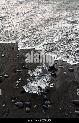 Iceberg fondu, cristal de glace sur la plage de lave noire, lavé par une vague, plage de diamants en été, Joekulsarlon, parc national de Vatnajoekull, Islande Banque D'Images