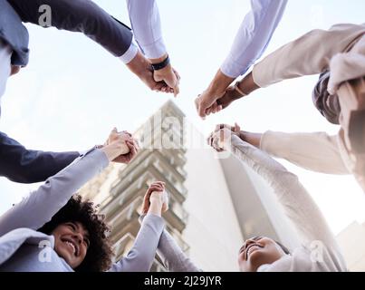 Nous l'avons fait. Spectacle sous angle d'un groupe diversifié d'hommes d'affaires qui se sont rassemblés à l'extérieur et ont tenu les mains. Banque D'Images