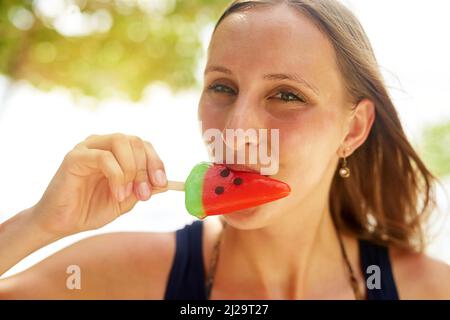 La meilleure façon de se rafraîchir cet été. Portrait d'une jeune femme attrayante profitant d'un popsicle sur la plage. Banque D'Images