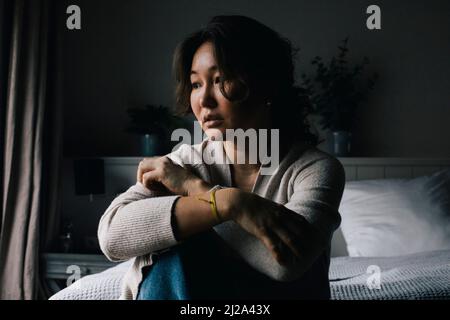 Femme seule déprimée assise sur le lit en regardant loin à la maison Banque D'Images