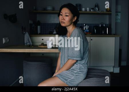 Femme émotionnellement stressée assise près d'une table à manger dans la cuisine à la maison Banque D'Images