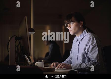 Jeune femme d'affaires utilisant l'ordinateur tout en travaillant tard dans le bureau la nuit Banque D'Images