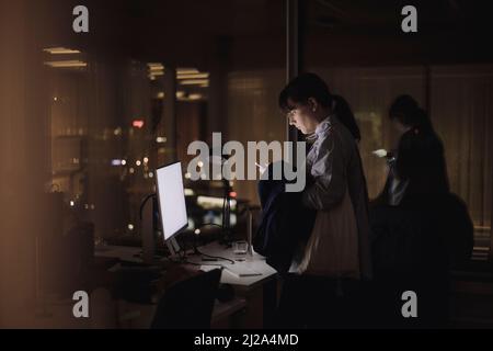 Femme d'affaires utilisant un smartphone tout en travaillant tard dans le bureau la nuit Banque D'Images