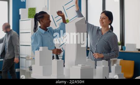 Équipe de femmes donnant les cinq hautes après le travail d'architecture progrès avec le modèle de construction. Architectes travaillant ensemble sur la conception et l'aménagement de la construction avec la maquette pour le projet urbain. Banque D'Images