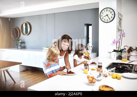 Rien de plus doux que le minuteur familial. Une jeune femme prend le petit déjeuner avec ses deux enfants. Banque D'Images