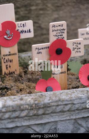 De petites croix de souvenir s'assoient contre un mémorial en pierre avec des coquelicots en papier décolorés. Banque D'Images