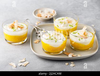 Délicieux plat de mangue maison et dessert en tranches de fromage à la crème, décoré de croustilles de noix de coco rôties et de zeste de citron vert râpé sur des verres. Banque D'Images