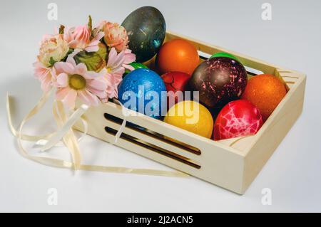 Composition de Pâques, oeufs colorés, peints à la main disposés dans une petite boîte en bois, encore la vie sur un fond clair, des fleurs Banque D'Images