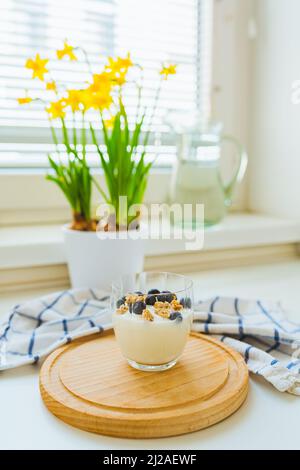 Le dimanche matin, yaourt diététique à petit déjeuner à faible teneur en calories avec myrtilles sauvages sur la table de cuisine. Fleurs printanières jonquilles, jour de congé le dimanche. Biologique sain Banque D'Images