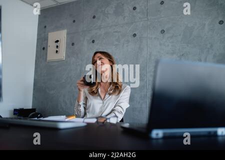 Femme d'affaires assise dans une chaise au bureau, aime le café d'une tasse noire, et pense.détente au travail dans un bureau moderne.elle sourit gentiment Banque D'Images