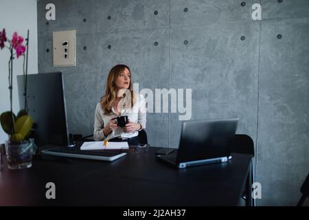Couche caucasienne, gestionnaire, exécutif, secrétaire femme tient la coupe noire dans les mains et regarde soigneusement par la fenêtre sur le côté gauche. Les notes sont à l'avant. Banque D'Images