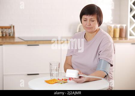 une femme âgée malade prend soin de la santé, en utilisant le sphygmomanomètre pour mesurer la pression artérielle, le pouls et la fréquence cardiaque par soi-même et prend des médicaments à la maison. Banque D'Images
