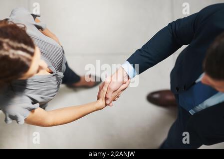 Bien accomplir quelques grandes choses ensemble. Prise de vue en grand angle de deux hommes d'affaires qui se secouent la main dans un bureau. Banque D'Images