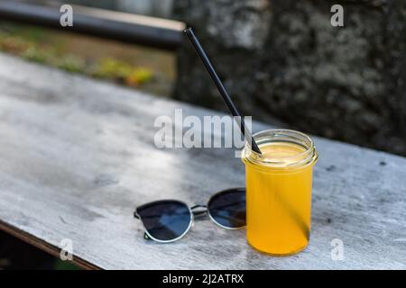 Un cliché sélectif d'un verre de jus avec une paille et une paire de lunettes de soleil sur le côté Banque D'Images