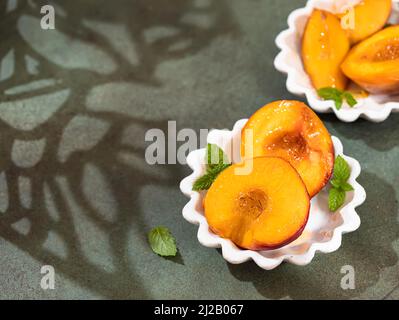 Pêches caramélisées au miel, avec feuilles de menthe sur fond de béton avec ombres. Dessert d'été. Copier l'espace Banque D'Images