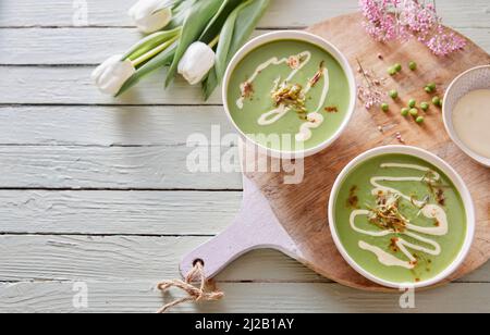 De la soupe de pois délicieuse dans des bols placés avec des fleurs de tulipe sur la table pour un déjeuner sain Banque D'Images