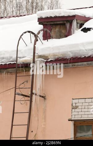 De longues glaces pendent du bord du toit. Sur le fond du mur d'une ancienne maison en briques. Grandes cascades, même de belles rangées. Jour d'hiver nuageux, lumière douce. Banque D'Images