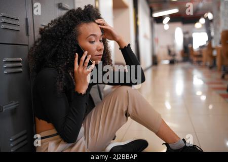 Un jeune étudiant fait un appel téléphonique sur le campus de l'université qui semble stressé, anxieux Banque D'Images