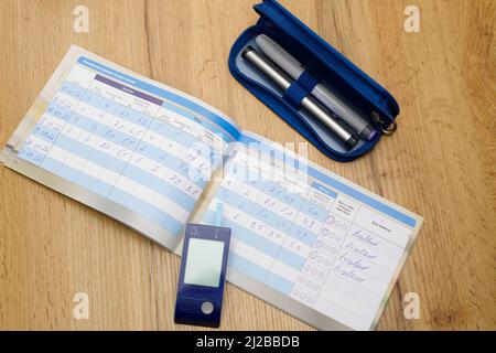 Gros plan d'un journal diabétique, d'un glucomètre et de stylos pour noter les données de mesure du taux de sucre dans le sang, concept diabétique. Banque D'Images