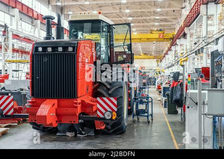 Gros tracteur ou moissonneuse rouge en cours d'assemblage en usine sur la chaîne de production pour la fabrication de machines agricoles. Banque D'Images