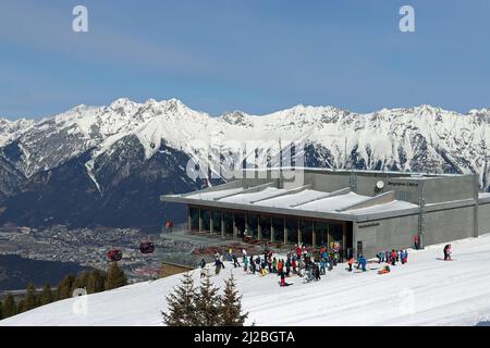 Les skieurs se rassemblent devant le restaurant Das Kofel à la station de montagne de Patscherkofelbahn, tandis que la télécabine s'élève au-dessus de la vallée de l'Inn et d'Innsbruck. Banque D'Images