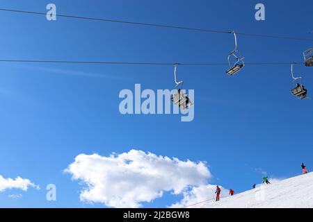 Une image générique d'un télésiège avec des skieurs au loin, dans un paysage enneigé, vu contre un ciel bleu vif et des nuages blancs moelleux (Autriche) Banque D'Images