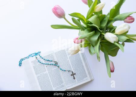 Bouquet de tulipes et rosaire bleu sur la bible ouverte sur fond blanc avec espace de copie Banque D'Images