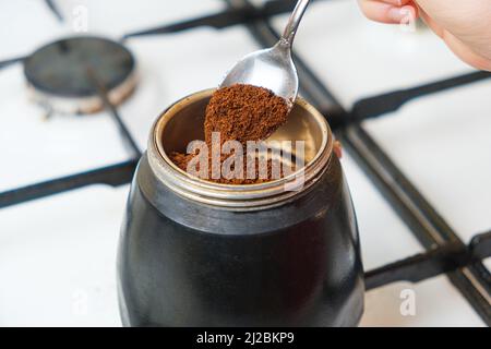 Le processus de verser le café moulu frais dans une machine à café geyser debout sur un poêle à gaz Banque D'Images
