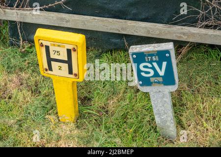 Un petit panneau indicateur de borne d'incendie encadré de béton à côté d'un panneau de barrière de luce monté similaire sur une bordure d'herbe Banque D'Images