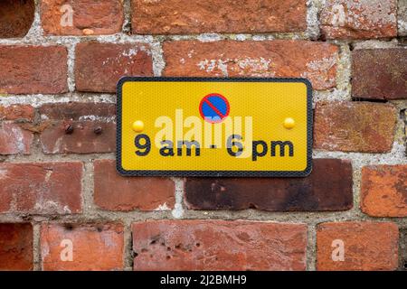 Petit panneau rectangulaire de restriction de stationnement noir sur jaune avec symbole rouge et bleu pour les heures de 9am à 6pm monté sur un mur de briques rouges Banque D'Images