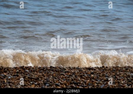 De petites vagues se brisent sur le rivage d'une plage de galets avec de la mousse blanche pétillante et une plage douce au premier plan Banque D'Images