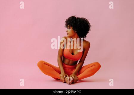 Belle femme afro-américaine méditant dans la tenue de sport sur fond rose portrait Banque D'Images