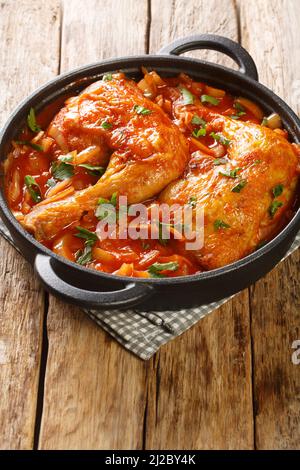 Pattes de poulet cuites dans une sauce tomate à l'oignon gros plan dans une poêle sur la table. Verticale Banque D'Images
