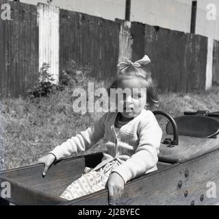 1961, à l'extérieur dans un terrain de jeu, une jeune fille assise dans un cheval à bascule en bois, Angleterre, Royaume-Uni. Un chapeau de sorcières peut également être vu. Le premier terrain de jeu au monde remonte à la mi-1800s, où un espace a été créé pour les enfants à jouer avec des blocs de bois et des jouets. Le terrain de jeu tel que nous l'avons connu aujourd'hui, développé comme un moyen d'encourager les enfants hors de la rue et à partir de 1930s, structures en bois et en métal, telles que les toboggans, balançoires, cadres d'escalade et manèges, a fourni un débouché pour les enfants à Amuse-toi bien. La montée des réglementations en matière de santé et de sécurité a vu de telles structures retirées du 1980s. Banque D'Images