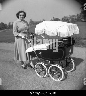 1950s, historique, à l'extérieur sur un chemin dans un parc, une dame dans une robe et des chaussures avec un entraîneur-construit pram ou voiture de bébé de l'époque, à l'ombre, Shrewsbury Park, Angleterre, Royaume-Uni. Un pram traditionnel construit par un entraîneur était un article populaire à cette époque, ayant de nombreux avantages pour la mère et l'enfant. Grâce à son châssis en acier robuste, sa suspension et ses grandes roues en fil métallique, il était léger à pousser, tandis qu'un matelas rembourré dans un landau solide et profond était synonyme de confort pour le bébé. Un avantage supplémentaire a été la position du bébé, en haut, face au parent, signifiait beaucoup de contact avec les yeux. Banque D'Images