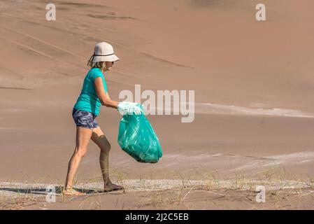 Femme mature dans un chapeau blanc et des gants verts collectant les ordures dans un sac vert. Blog concept Banque D'Images