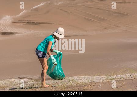 Femme mature dans un chapeau blanc et des gants verts collectant les ordures dans un sac vert. Blog concept Banque D'Images