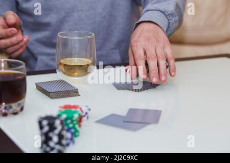 Les mains de l'homme permettent de mélanger des cartes. Jeu de poker avec jetons, cartes sur la table. Verre de whisky. Profitez de l'instant, détoxication numérique avec vos amis. Photographie de style de vie. Moment sincère. Mise au point sélective Banque D'Images