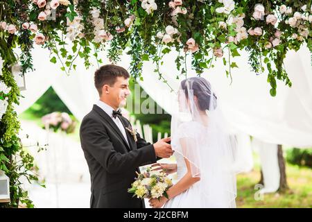 Couple de mariage sous l'arche de fleur à la cérémonie de mariage à l'extérieur dans le parc Banque D'Images