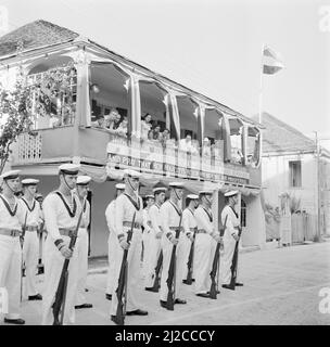 Des marins attendent à Philipsburg sur Sint Maarten devant une maison avec une bannière. L'inscription se lit comme suit: Avec des coeurs loyaux et vrai, le peuple de Sint Maarten accueille sa gracieuse majesté la reine Juliana et le prince Bernhard et prie pour que le règne de sa majesté soit long et prospère ca: 25 octobre 1955 Banque D'Images