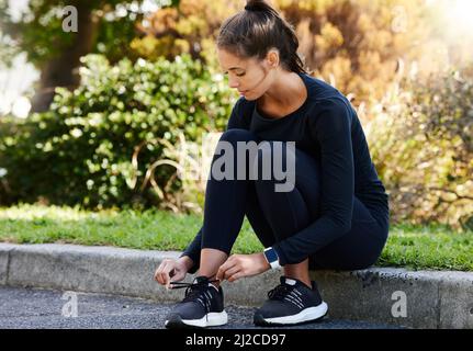 Assurez-vous que ses lacets sont bien serrés. Prise de vue en longueur d'une jeune femme attirante et athlétique qui noue ses lacets tout en étant assise sur le trottoir Banque D'Images