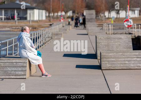 Femme en peignoir reposant sur un banc après un bain de printemps tôt dans la mer Banque D'Images