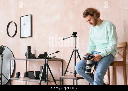 Photographe masculin avec appareil photo assis dans une chaise près du mur rose dans un studio moderne Banque D'Images