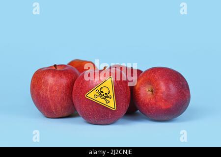 Pommes rouges avec étiquette du symbole du crâne de poison sur fond bleu. Notion de résidus de pesticides dans les aliments agricoles Banque D'Images