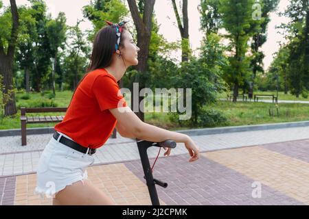 E-bike, sécurité des scooters. Jeune femme à cheval en milieu urbain. Femme à la mode en scooter électrique dans le parc de la ville Banque D'Images