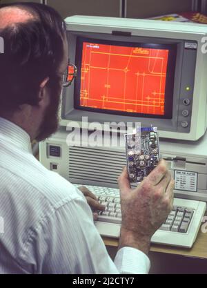 SYRACUSE, NEW YORK, Etats-Unis - Man at Computer Works on Computer-aided design, février 1987. L'écran de l'ordinateur affiche le schéma de la carte en main. Banque D'Images