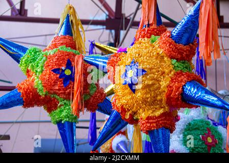 Deux pinatas colorées en forme d'étoiles suspendues à l'extérieur d'un magasin de fournitures de fête. San Miguel de Allende, Guanajuato, Mexique. Banque D'Images