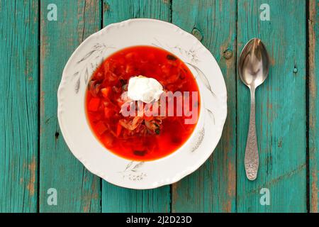 Soupe russe de betteraves rouges borscht à la crème aigre dans une assiette blanche sur table turquoise vue de dessus Banque D'Images