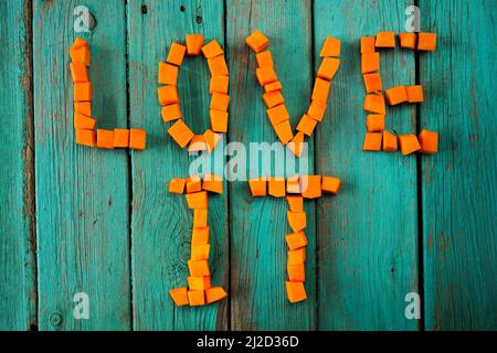 Mots Love il écrit avec des cubes de citrouille brute sur table en bois turquoise vue du dessus Banque D'Images